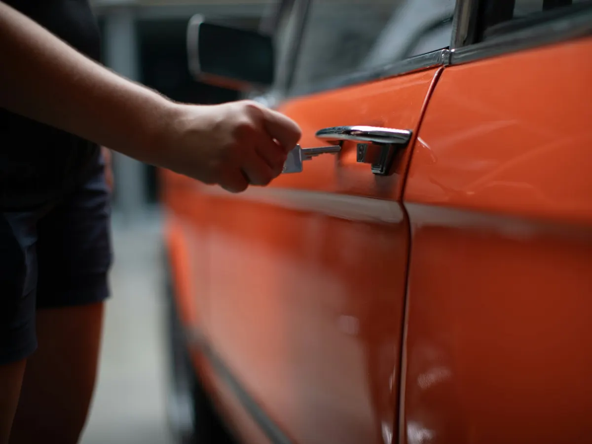 A hand putting a key into the door lock of an orange car.