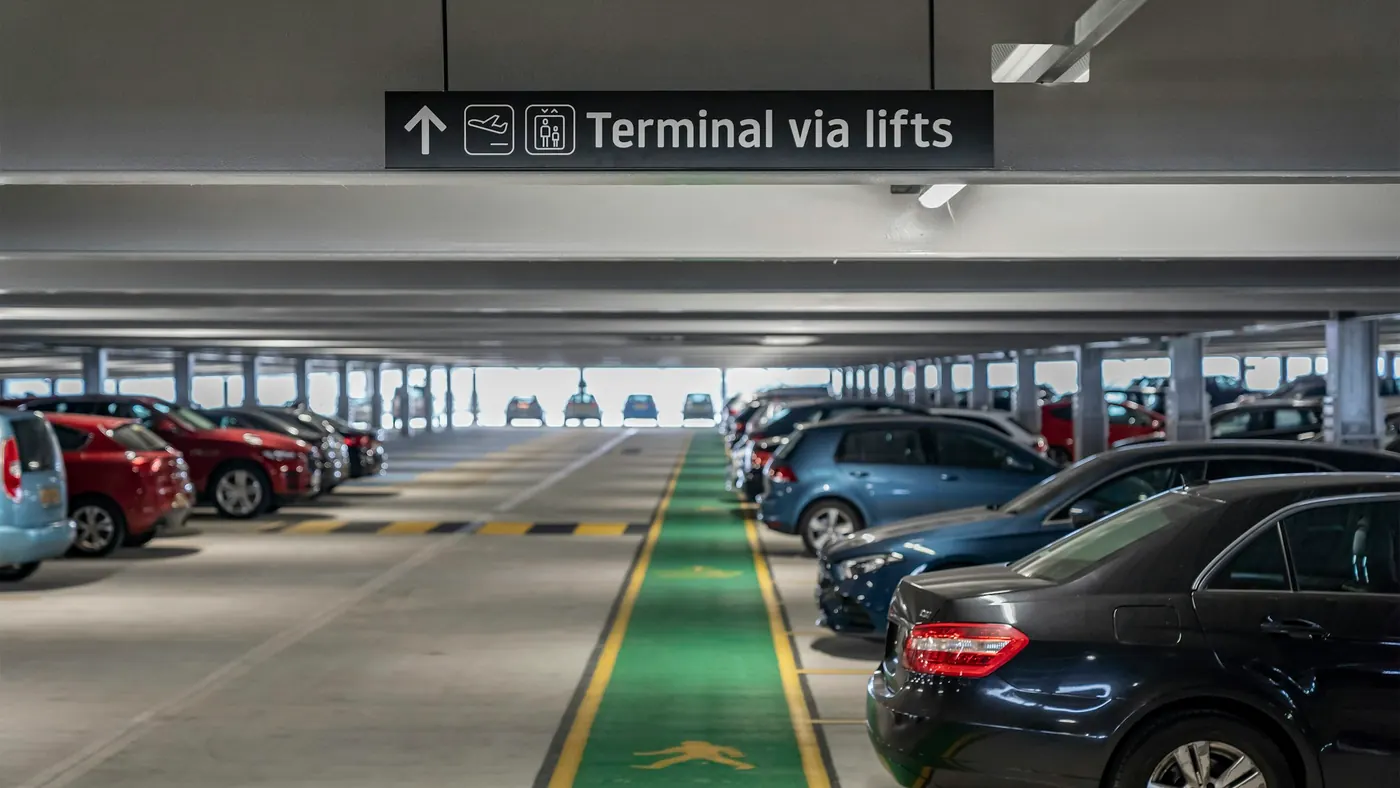 Rows of parked cars inside an airport car park, under a sign pointing the way to the terminal.