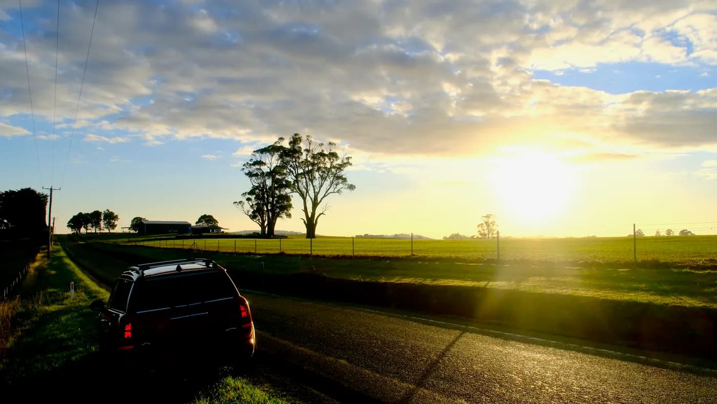 A vehicle parked on the verge of an open road at sunset.
