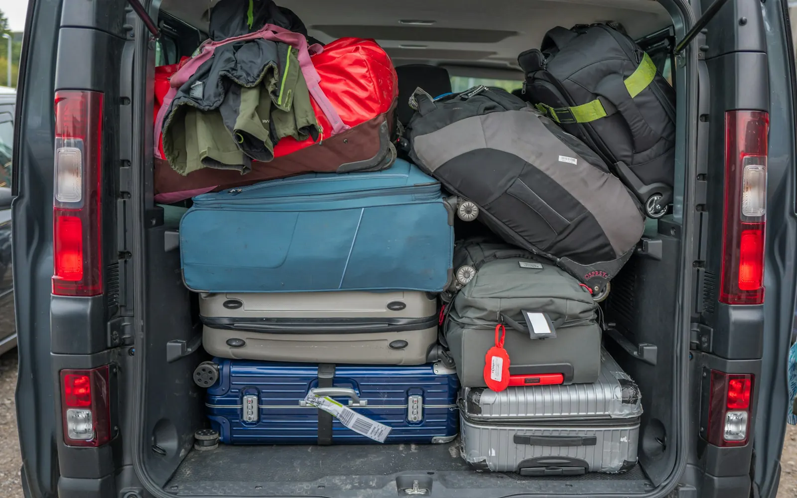 The open rear doors of a van, its hold packed to the roof with suitcases and holdalls.