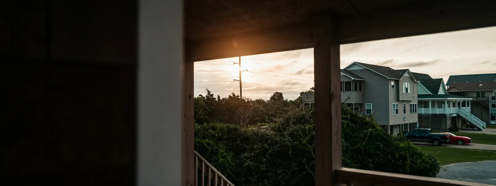 A covered porch at sunset, looking out past the posts to neighbouring houses and vehicles parked on the street.