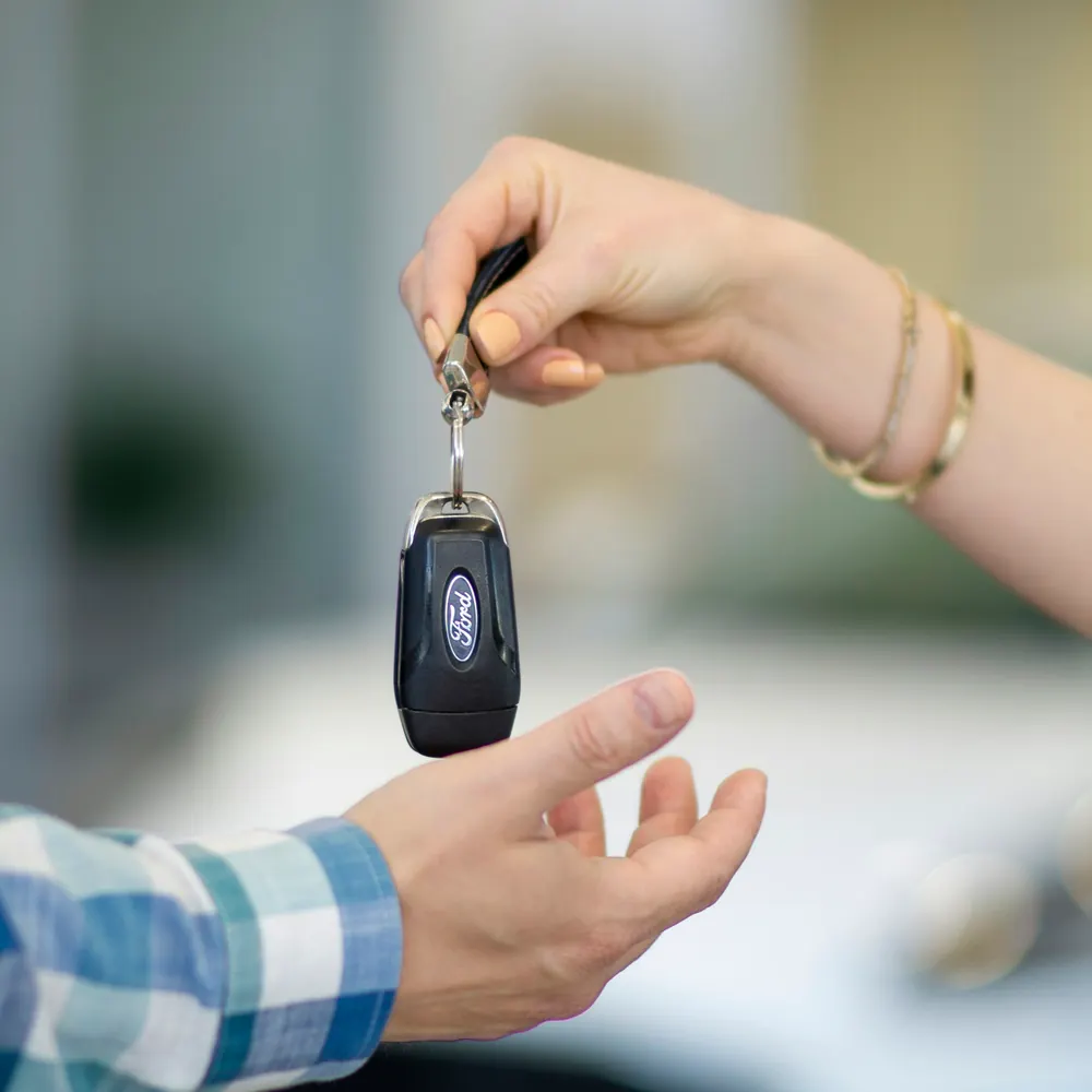 A set of car keys passed from one hand to another beside a parked car.